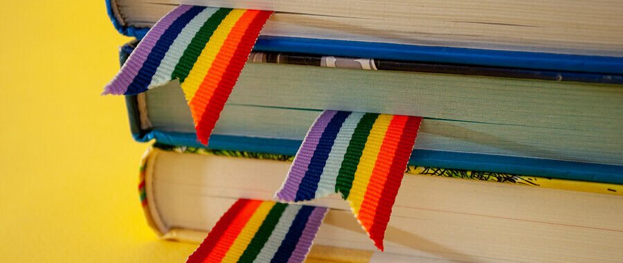 A Stack Of Three Books With Rainbow Ribbon Bookmarks Is On The T